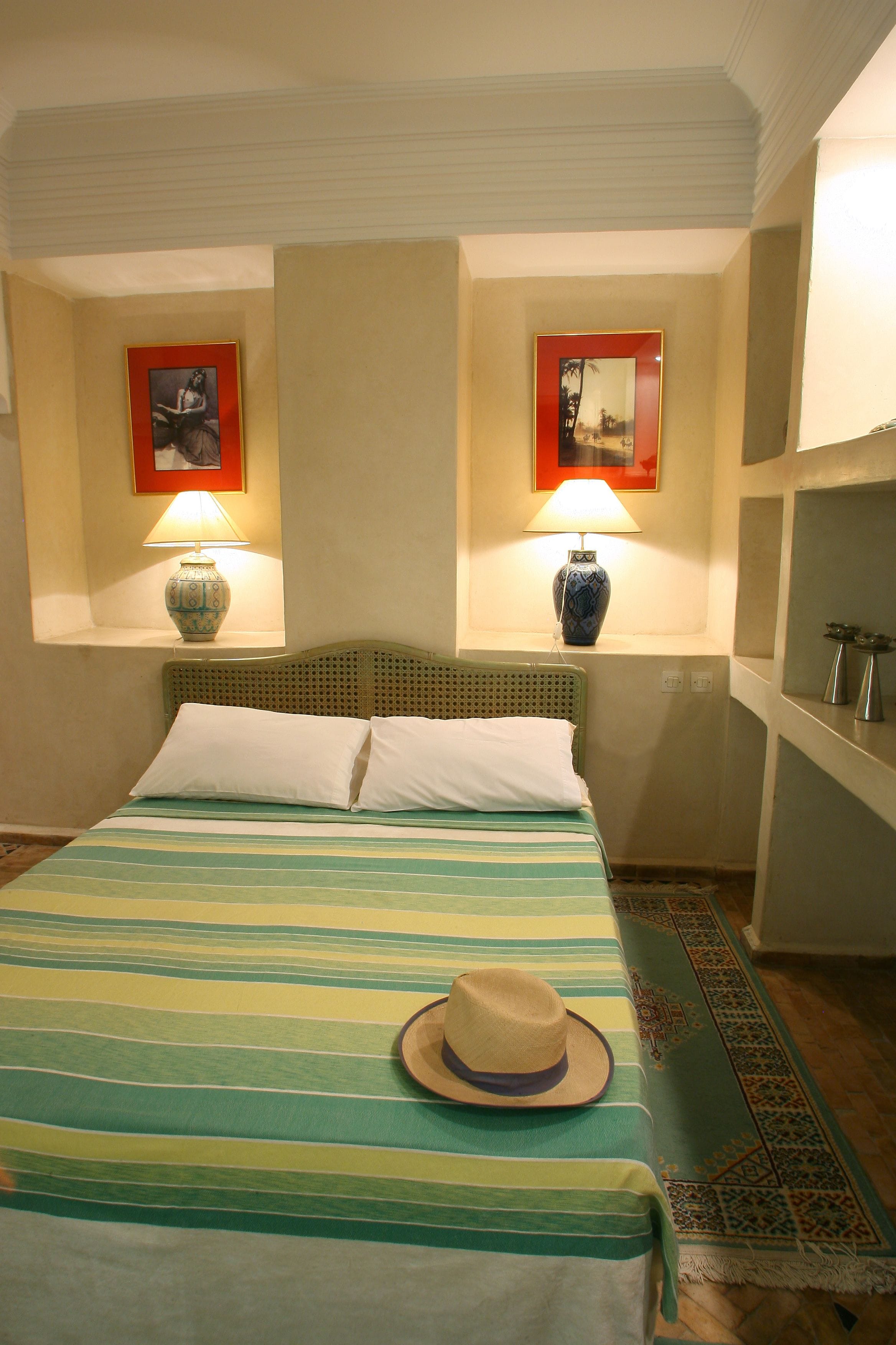 A bed with striped bedding, a hat on the bed, two wall-mounted lamps, and a framed picture above each lamp.