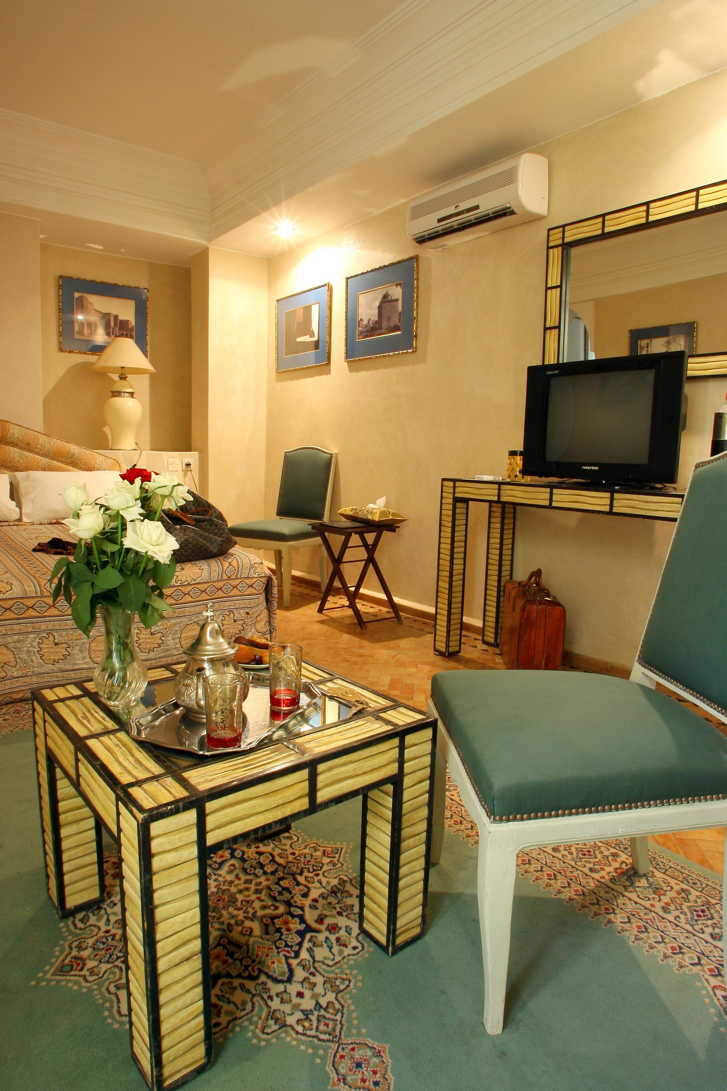 A living room with a sofa, a green armchair, a coffee table, a television, and a wall-mounted air conditioner.