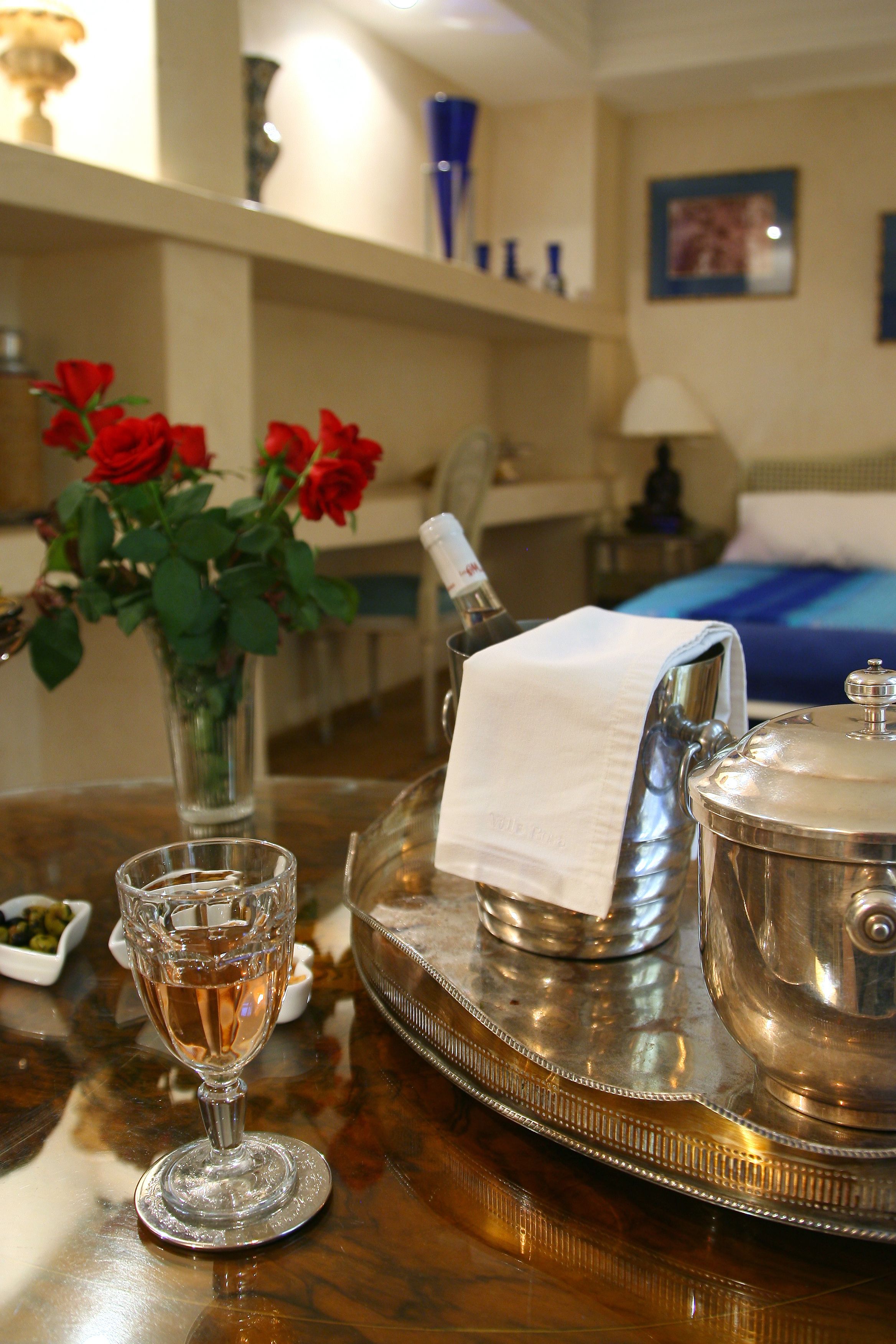 A tray with a silver teapot and a glass of water, a vase with red roses, and a small bowl of olives on a wooden table.