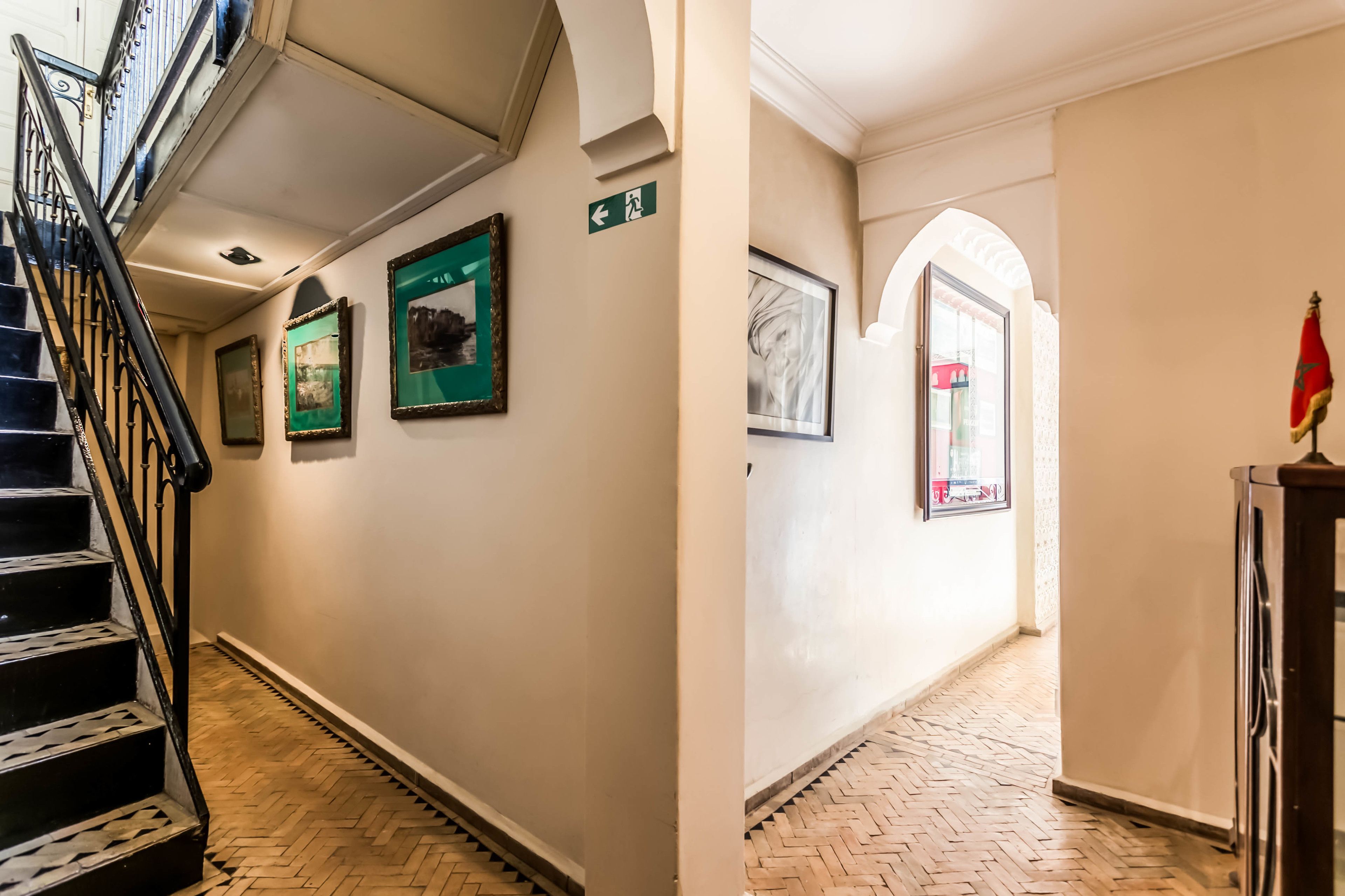 A hallway with a wooden herringbone floor, a staircase with black railings, and framed pictures on the walls.