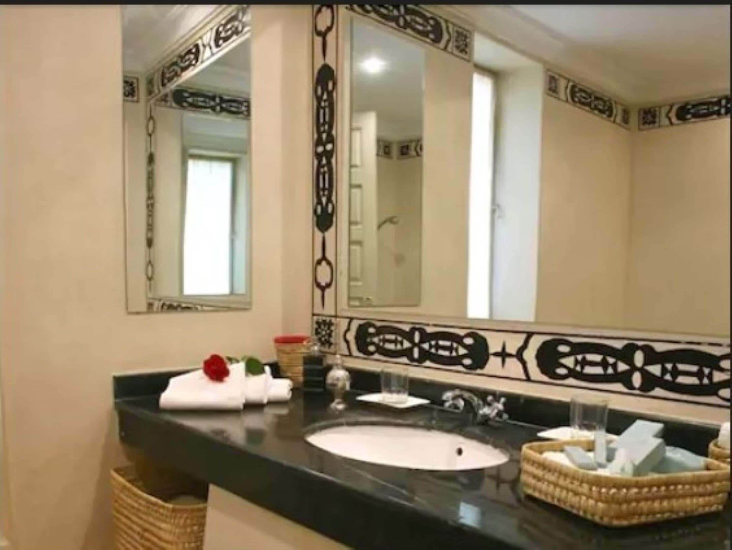 A bathroom with a black countertop, a white sink, and a large mirror with decorative borders.