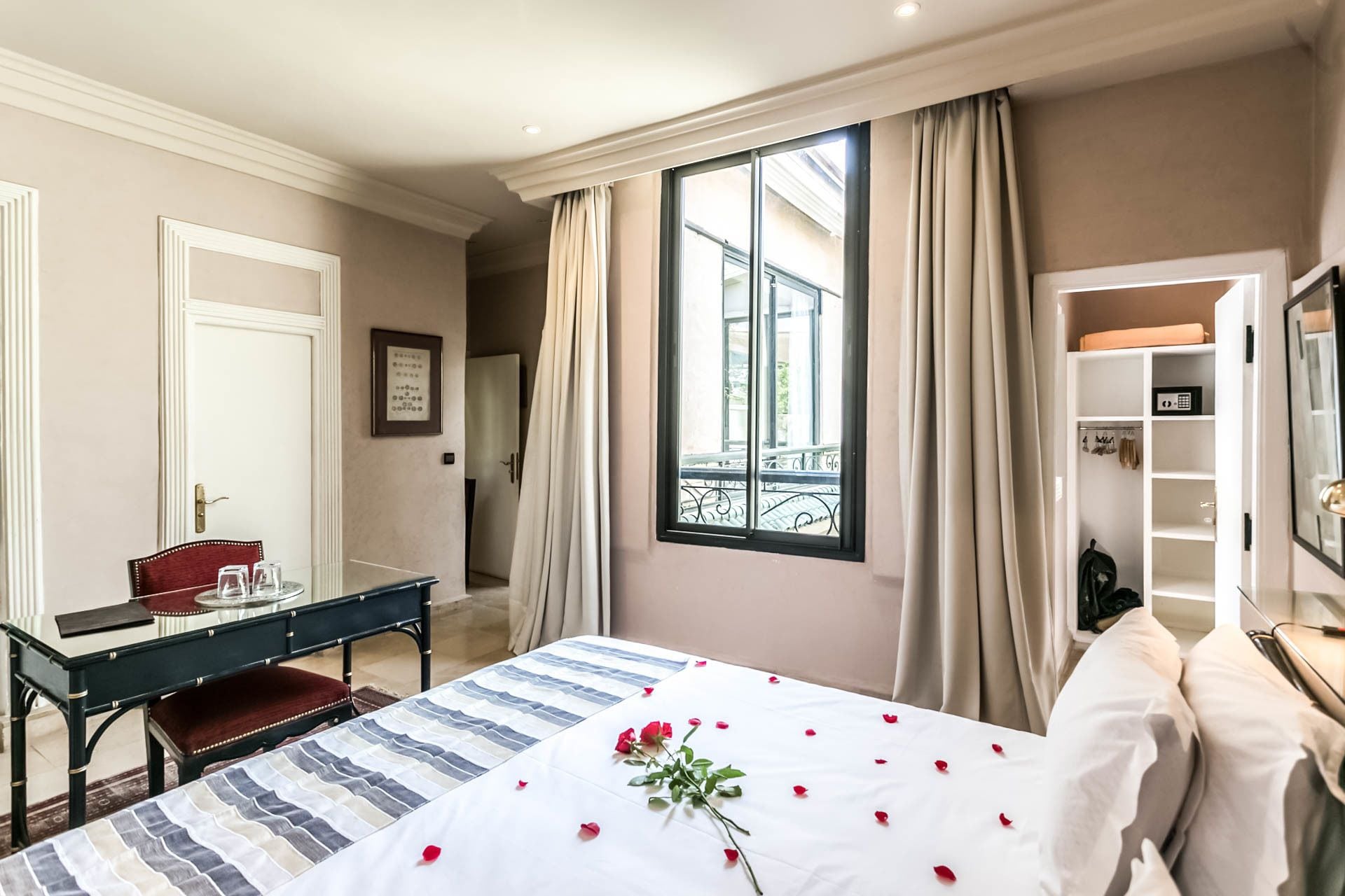 A hotel room with a bed, a desk, a chair, a wardrobe, and a window with curtains.