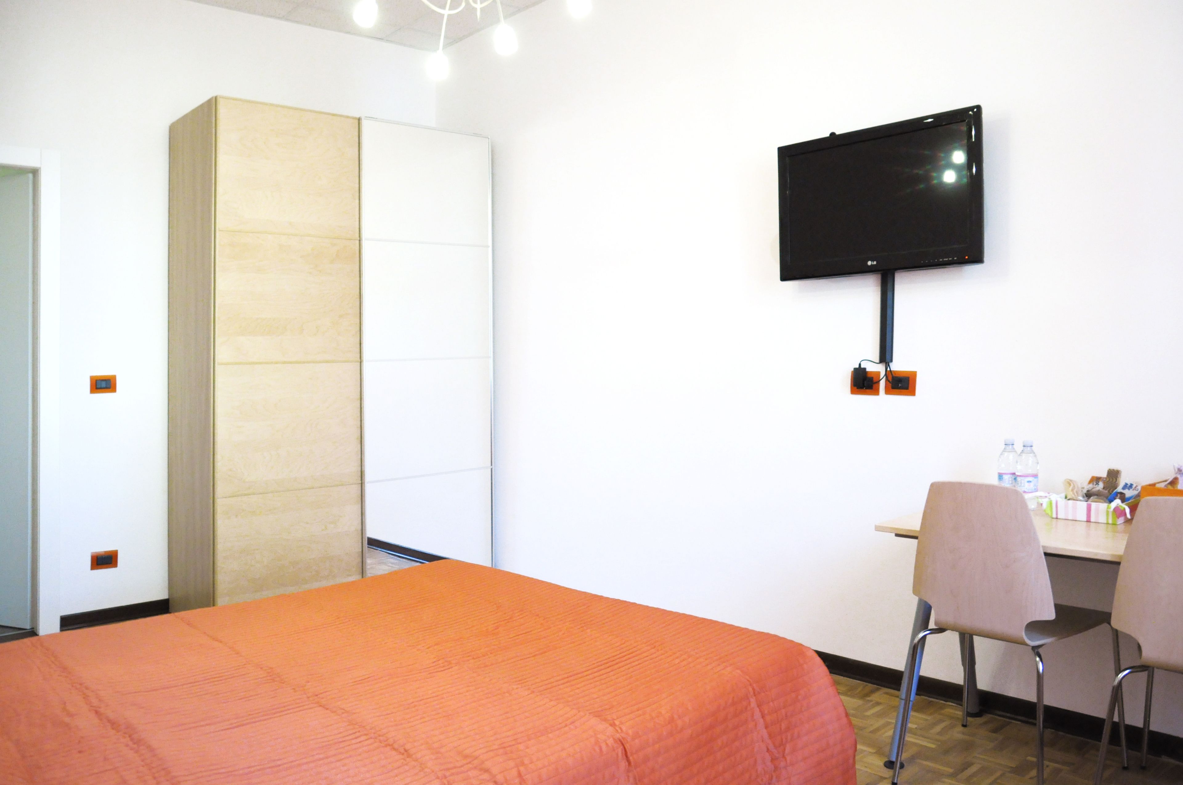 Una habitación de hotel con una cama, un escritorio, dos sillas, un televisor y un armario.