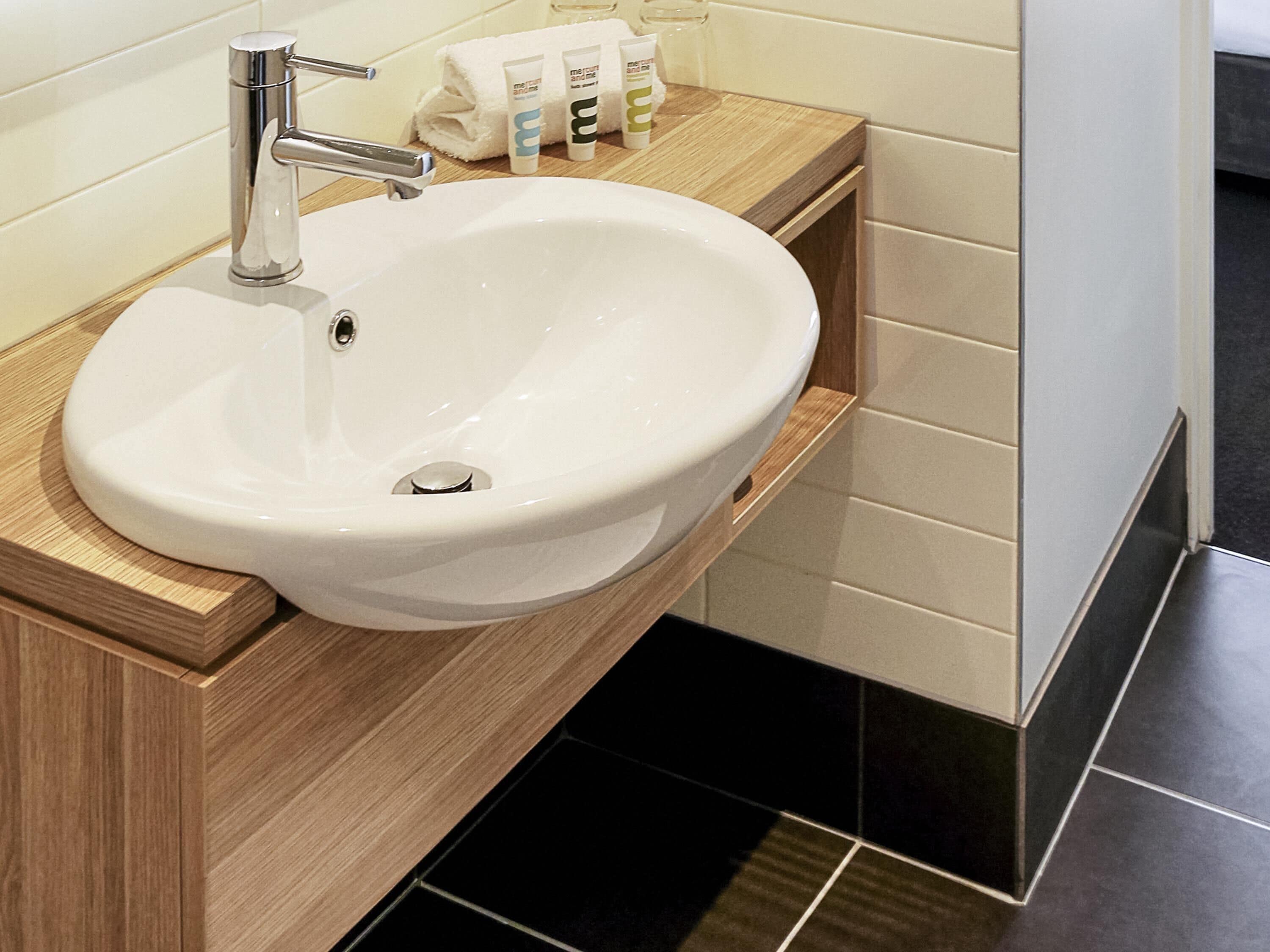 A white bathroom sink with a chrome faucet, a wooden vanity, and black tiled flooring.