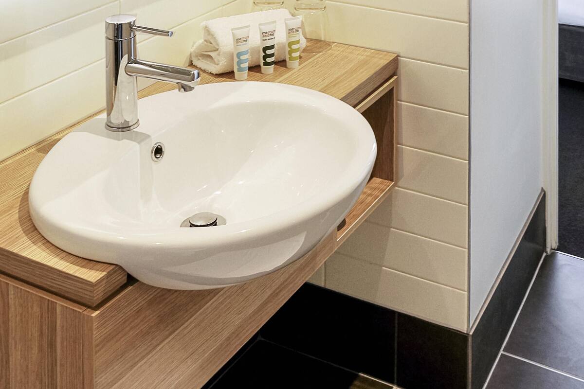 Ein weißes Waschbecken mit chromfarbenem Wasserhahn, ein Holzschrank und schwarze Fliesenböden.
