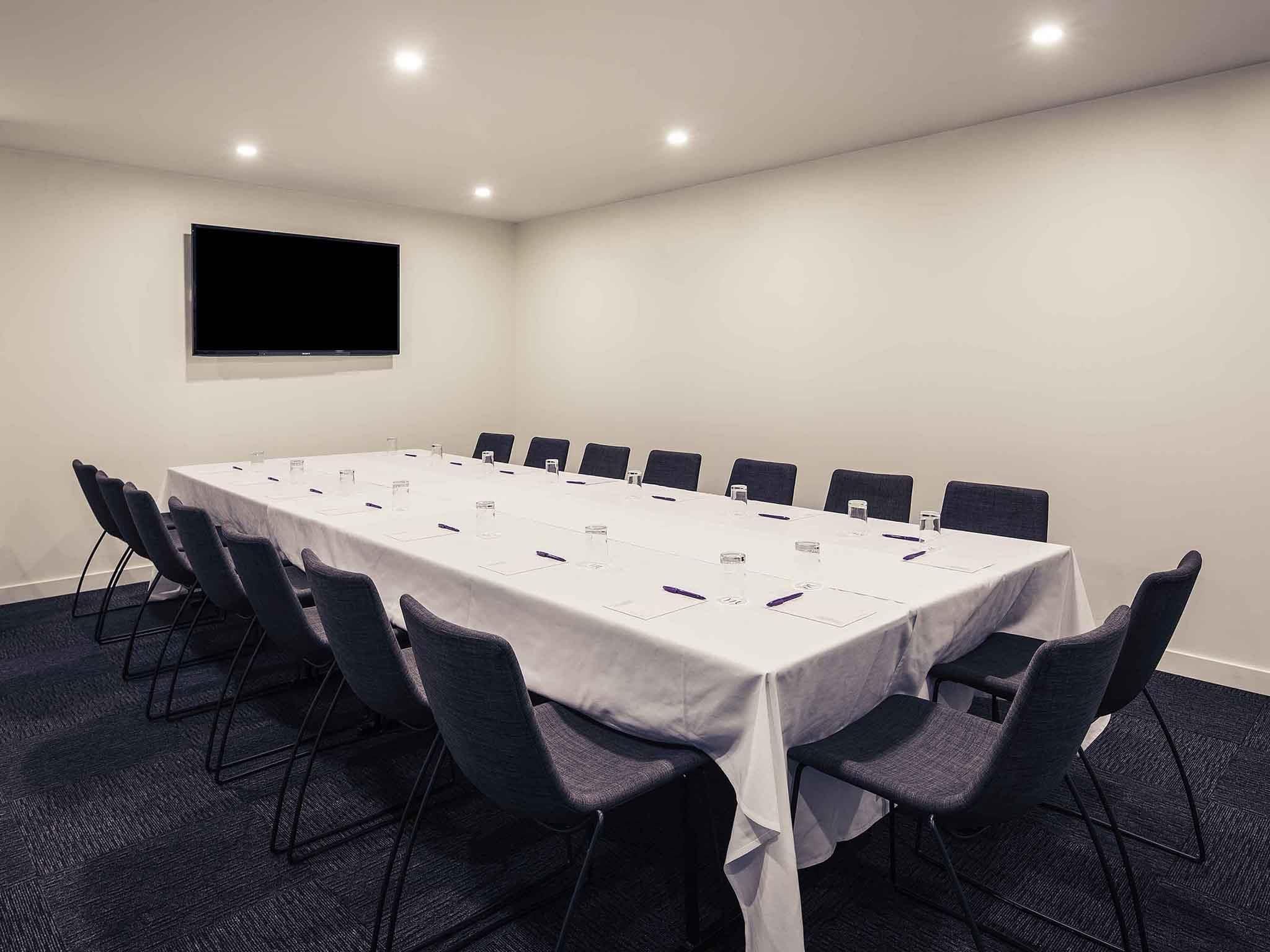 A conference room with a long table, chairs, a flat-screen TV, and a white tablecloth.