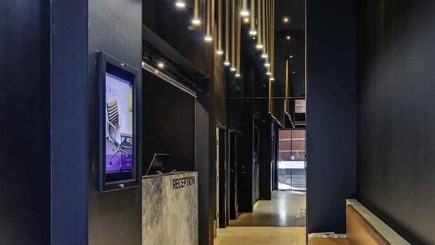 A modern reception area with a reception desk labeled "RECEPTION," a digital screen displaying information, and a hallway leading to another section. - Mercure Melbourne Therry Street (Melbourne)