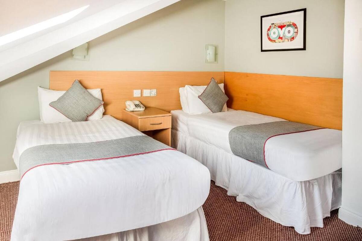 A hotel room with two beds, a wooden headboard, a telephone, and a framed picture on the wall.