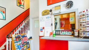 A reception desk with a red and white color scheme, a clock, and a sign indicating check-out times. - London Guest House by OYO - Acton (London)