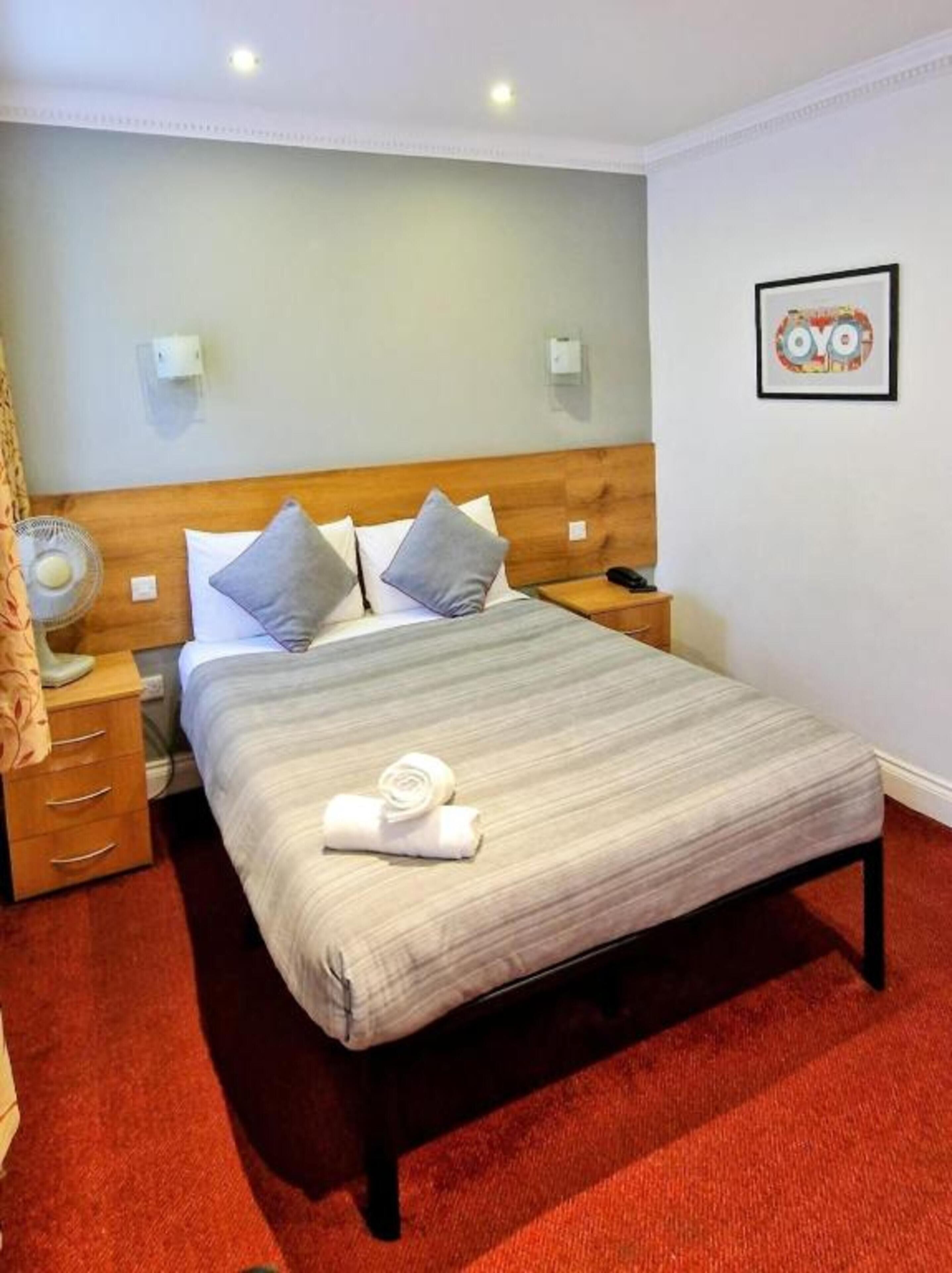 Habitación de hotel con cama, mesita de noche, lámpara de pared e imagen enmarco.