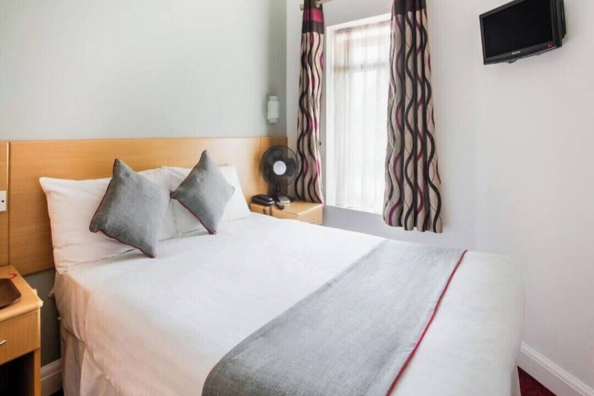 A hotel room with a bed, pillows, a bedside table, a TV, and curtains.