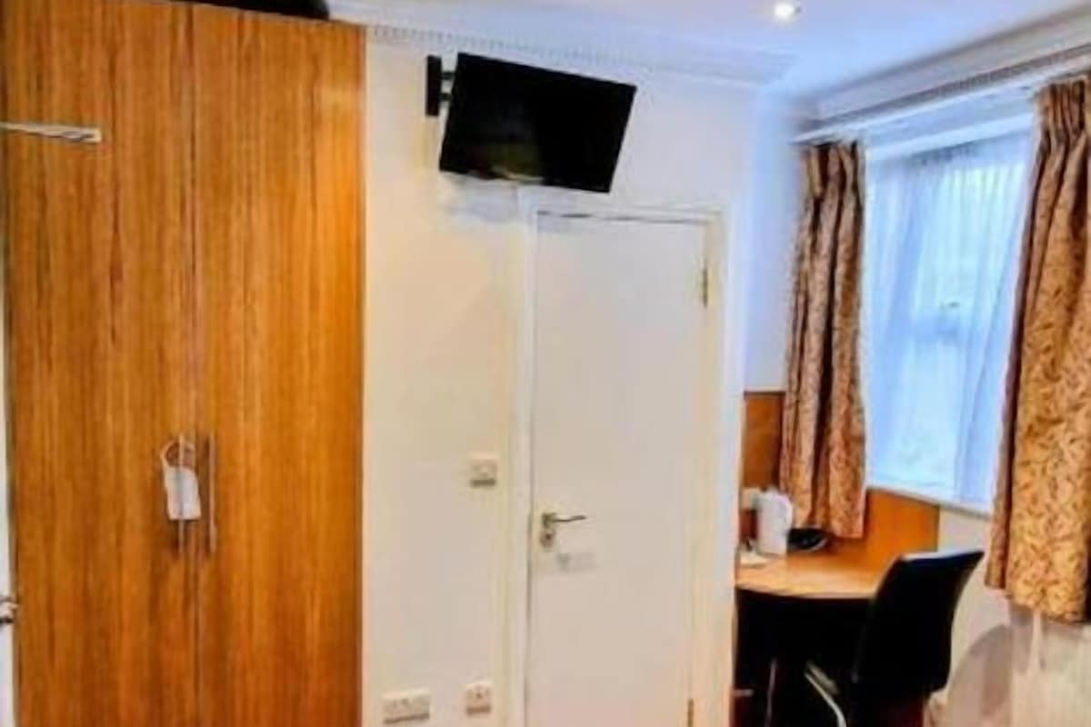 A hotel room with a bed, a desk, a television mounted on the wall, and a wardrobe.