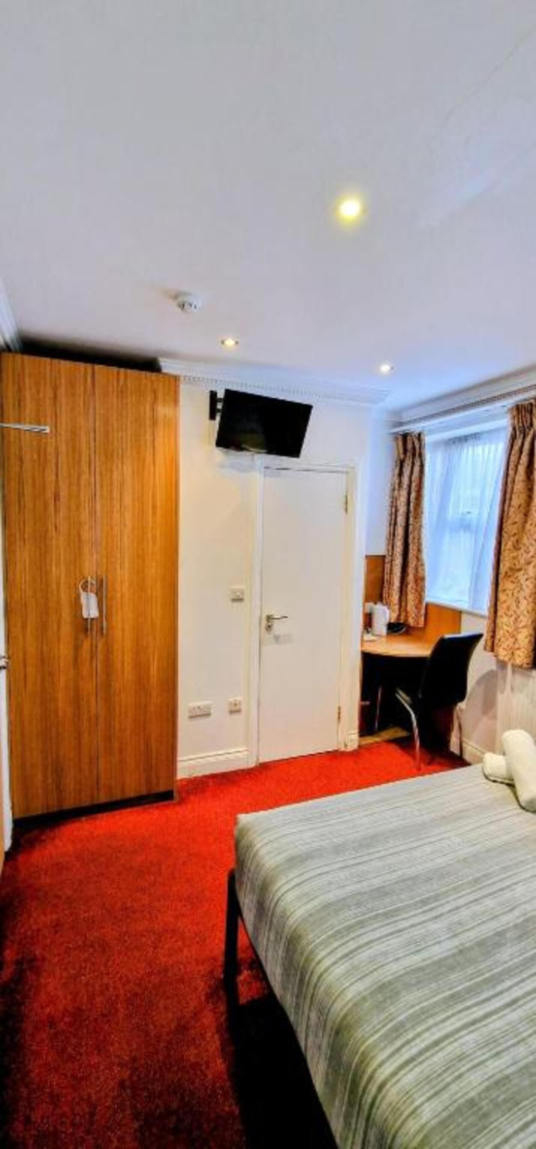 A hotel room with a bed, a desk, a television, and a wardrobe.
