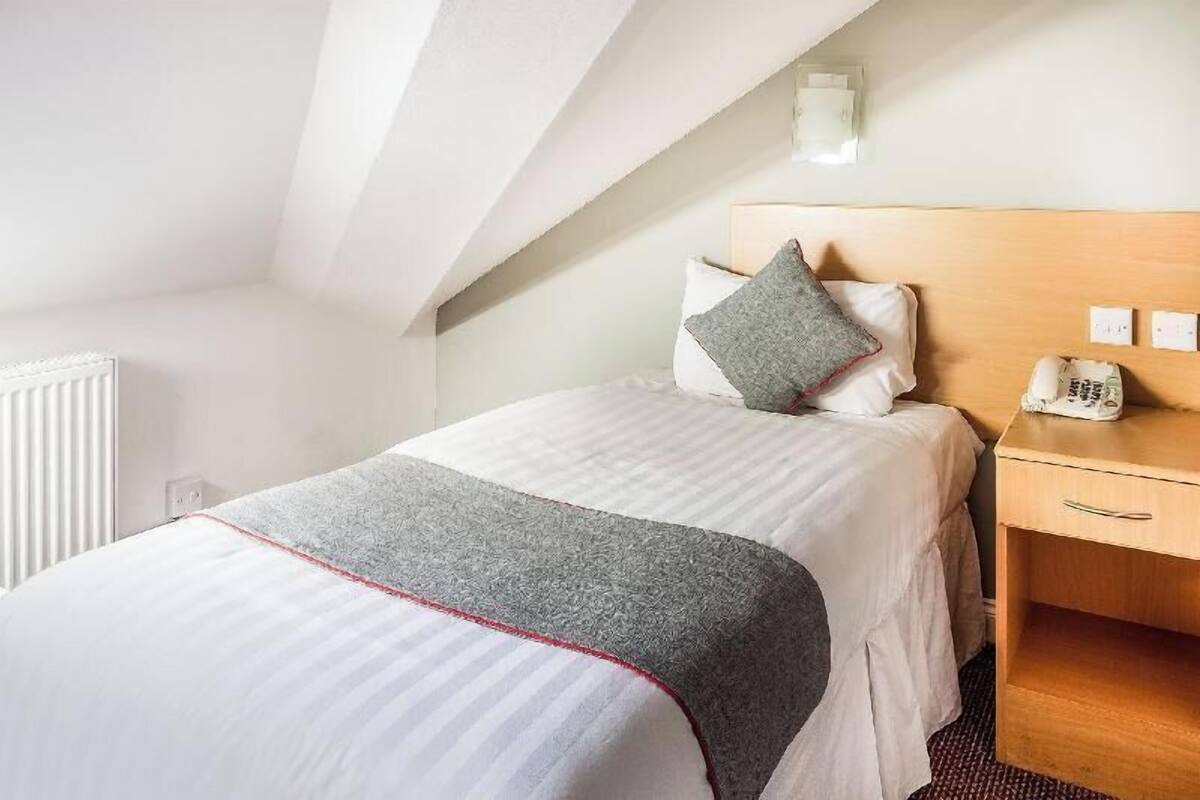 A hotel room with a bed, a bedside table with a phone, and a radiator.