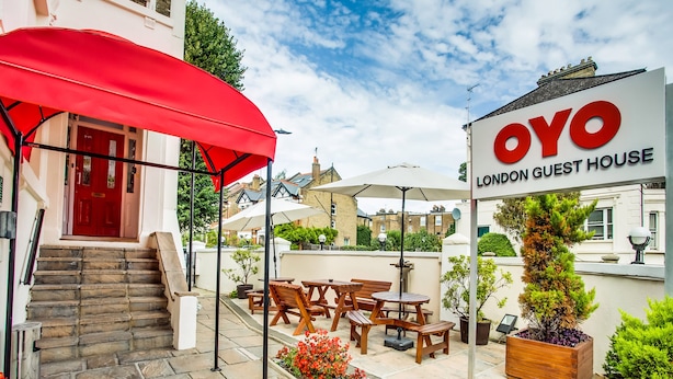 A London guest house with outdoor seating, a red umbrella, and a signboard. - London Guest House by OYO - Acton (London)