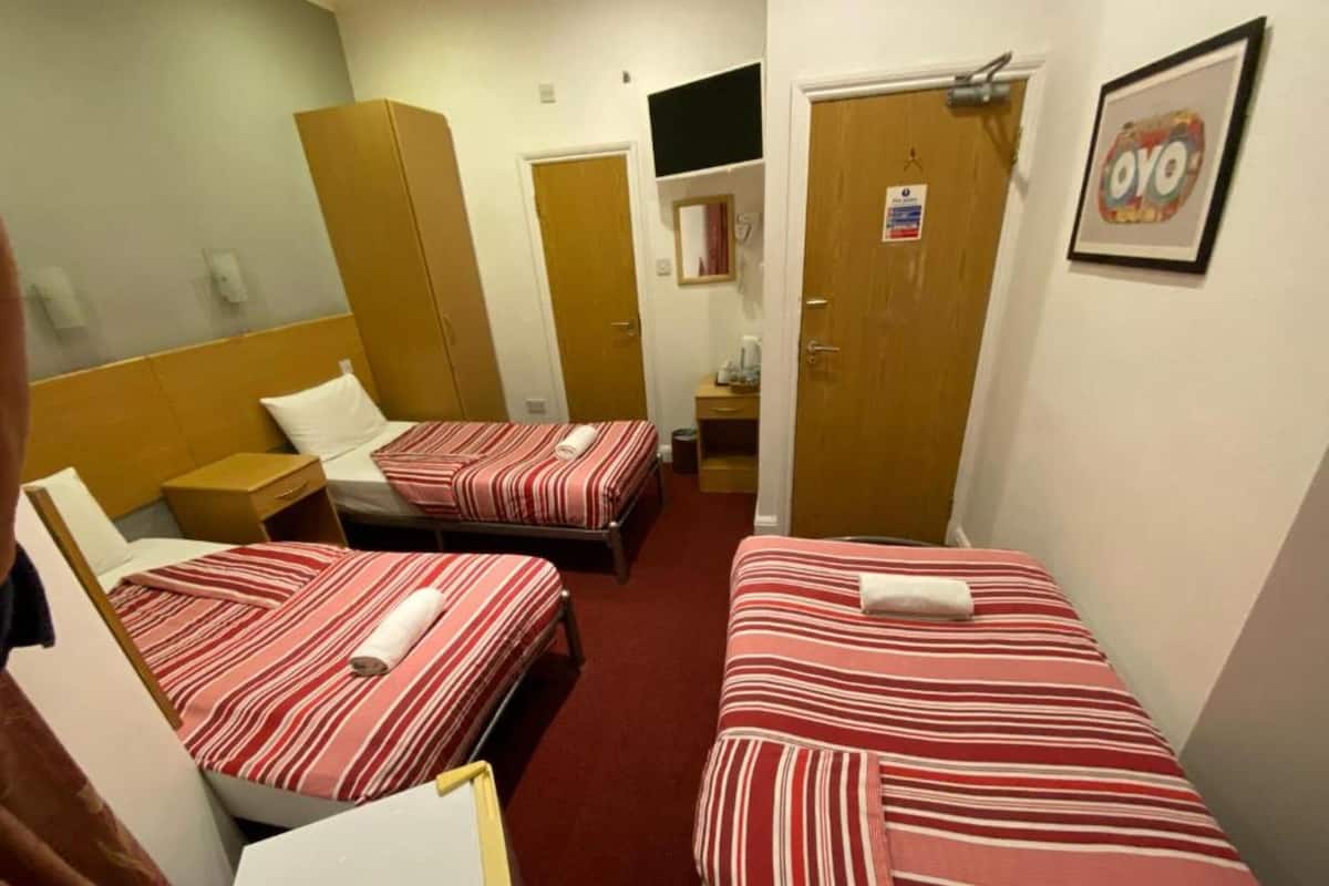 A hotel room with two single beds, a wooden wardrobe, a desk, and a small table.