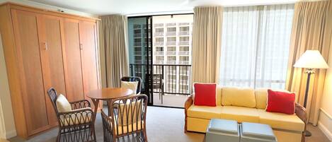 A hotel room with a sofa, armchair, table, and wardrobe.