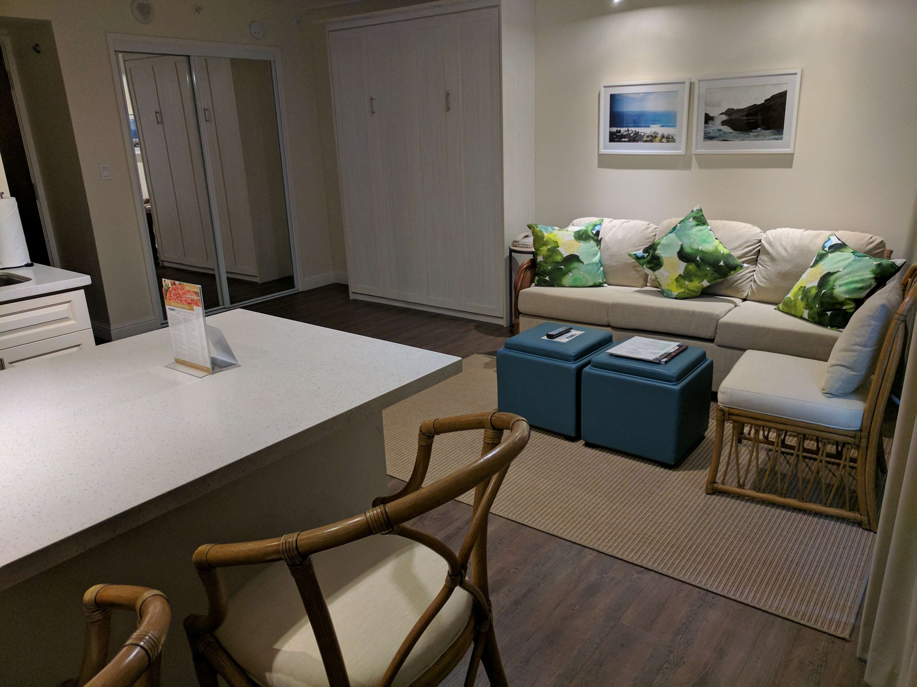 A modern living room with a sofa, two blue ottomans, a wooden chair, and a white coffee table.