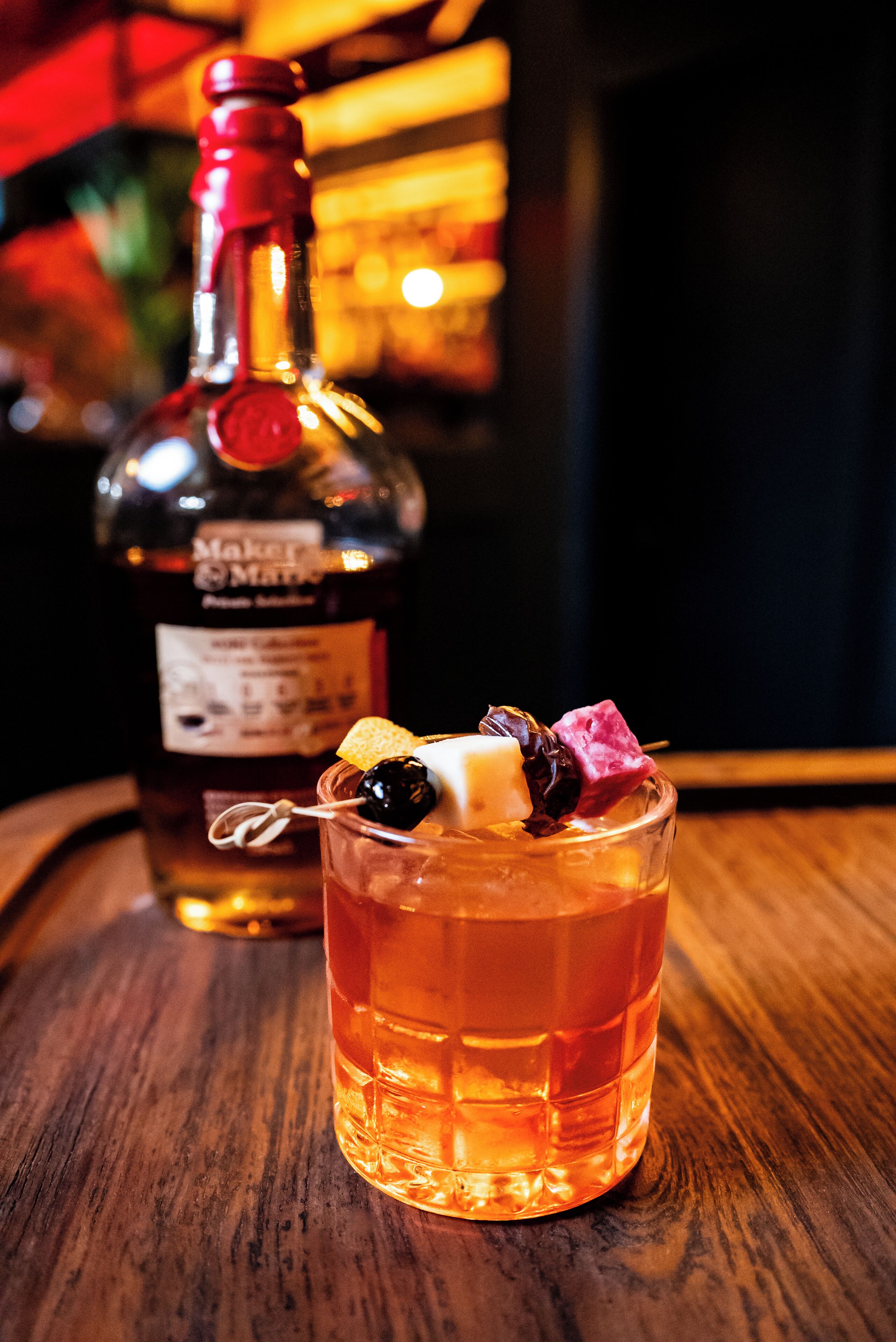 A bottle of Maker's Mark whiskey and a glass with a cocktail on a wooden surface.