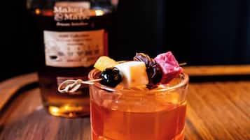 Una botella de whisky Maker's Mark y un vaso con un cóctel sobre una superficie de madera.