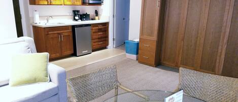 A compact living space with a kitchenette, a sofa, a glass coffee table, and a dining area.