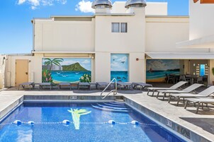 Piscina con sillones de descanso y un mural que representa una playa.