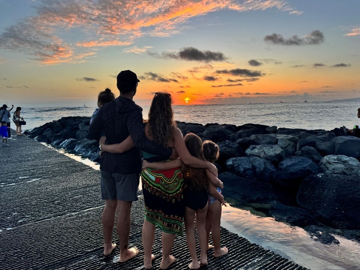 Una familia de cuatro personas sobre un muelle rocoso al atardecer.