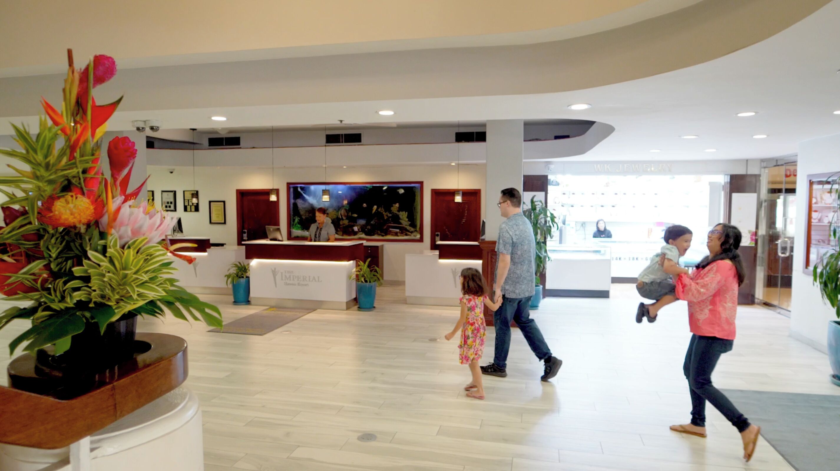 A spacious lobby with a reception desk, potted plants, and a large painting on the wall.