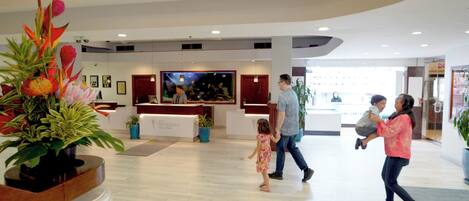 Eine großzügige Lobby mit einer Rezeption, Zimmerpflanzen und einem großen Gemälde an der Wand.