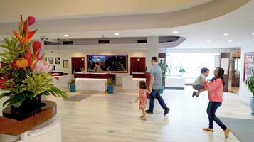 A spacious lobby with a reception desk, potted plants, and a large painting on the wall.