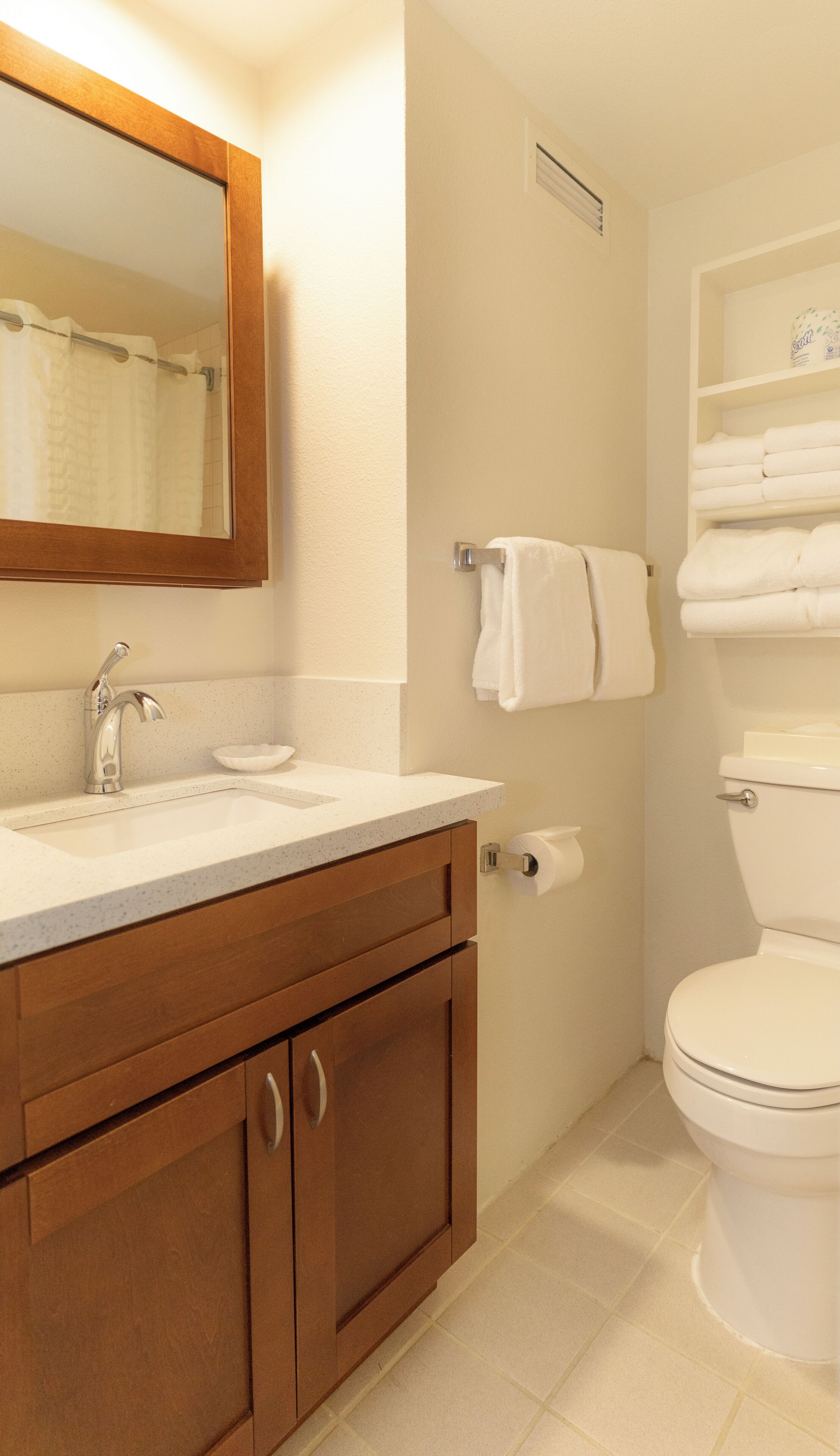 Un baño con tocador de madera, lavabo, espejo, inodoro y perchero para toallas.