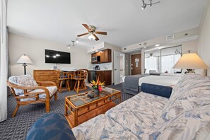A hotel room with a sofa, armchair, dining table, and chairs. There is a ceiling fan, a flat-screen TV, and a kitchenette with a microwave. - The Imperial Hawaii Resort (Honolulu)