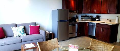 A compact living space with a kitchenette, a sofa with cushions, a dining table with chairs, and a ceiling fan.