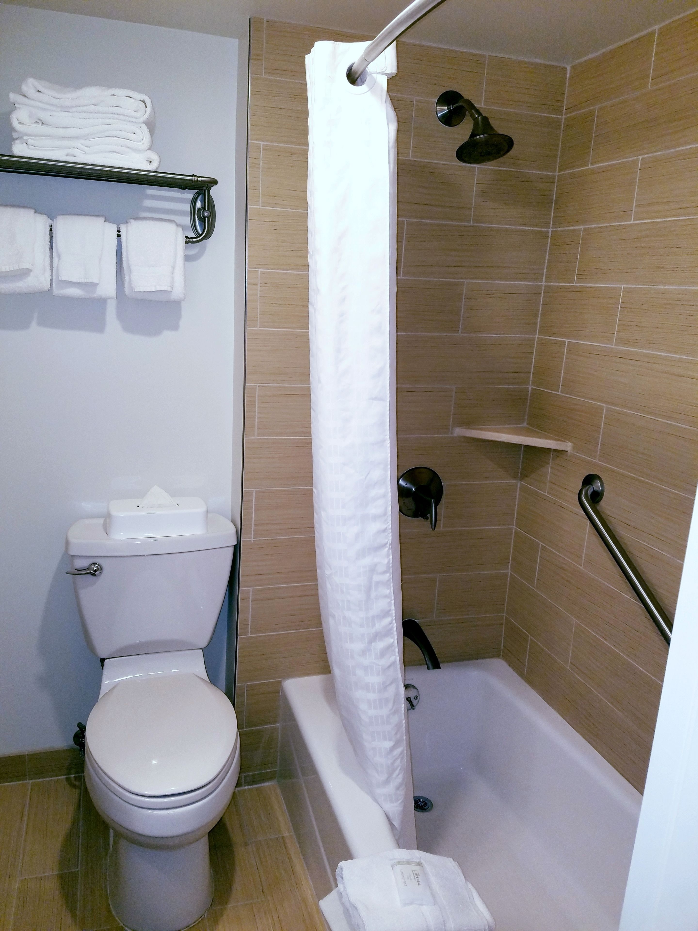 A bathroom with a toilet, a shower with a white curtain, and a towel rack with folded towels.