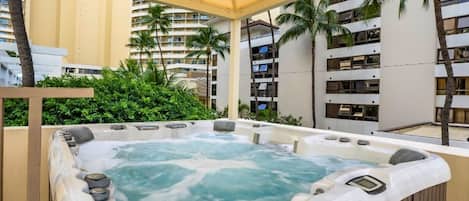 A hot tub area with a canopy, surrounded by palm trees and a building in the background.