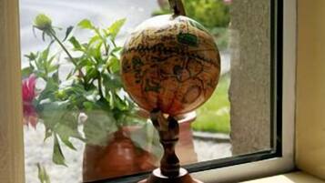 A globe on a wooden stand by a window with a view of greenery and a road.