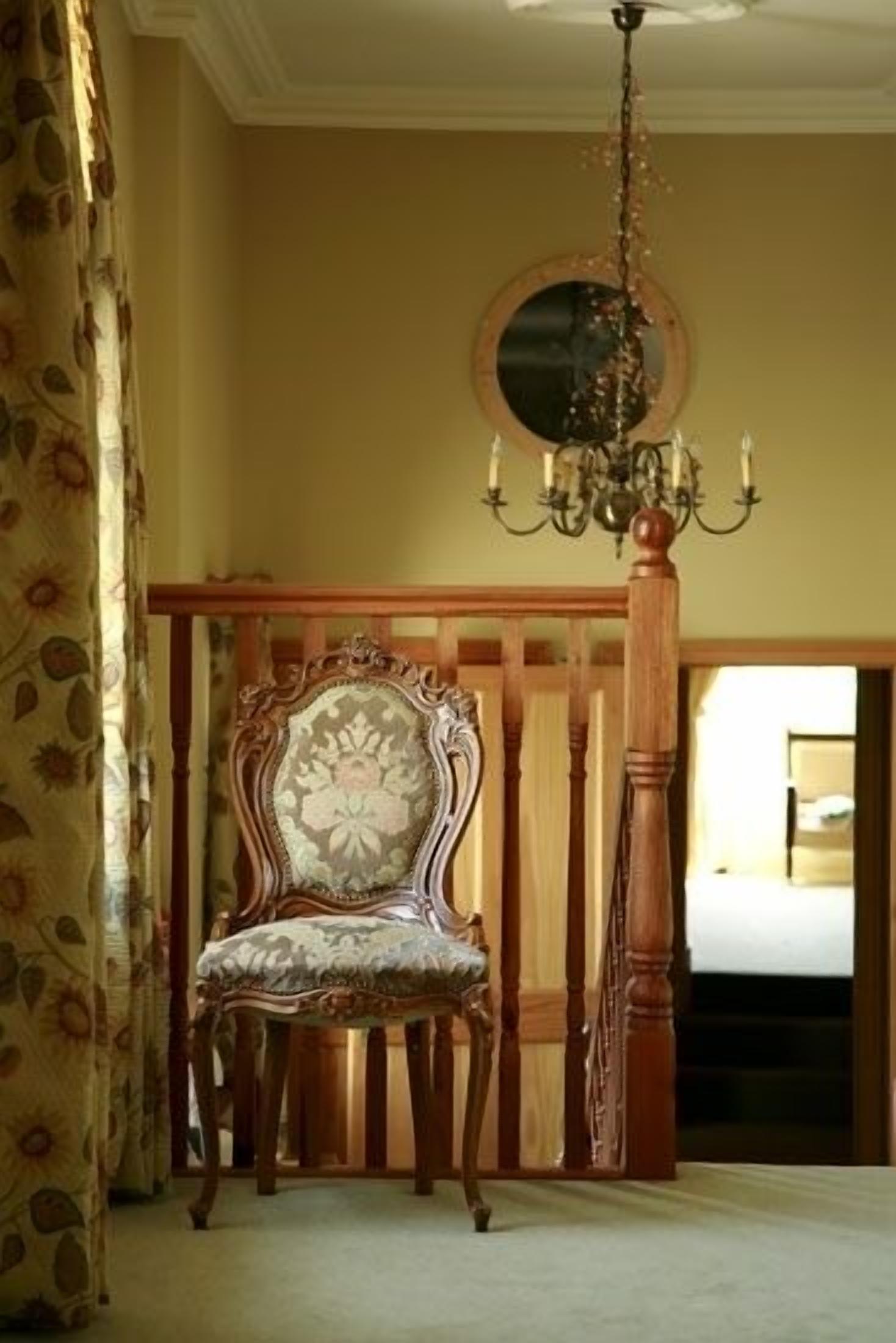 Quarto com uma cadeira de madeira, um candelabro e um espelho na parede.