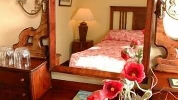 A bedroom with a wooden bed, a mirror, a nightstand, a lamp, and a vase with flowers.