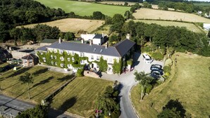 An aerial view of a large, multi-story building with a central courtyard, surrounded by green fields and trees. - Glendine Country House (Arthurstown)
