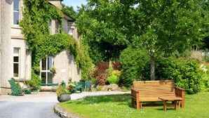 A stone building with ivy, a wooden bench, and a garden with various plants. - Glendine Country House (Arthurstown)