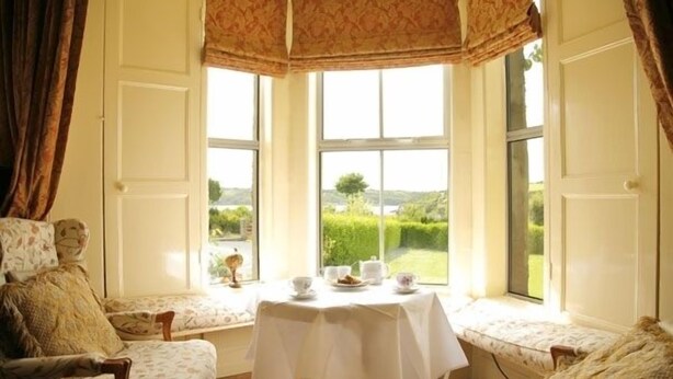A cozy room with a large window, a table set for tea, and a comfortable seating area. - Glendine Country House (Arthurstown)