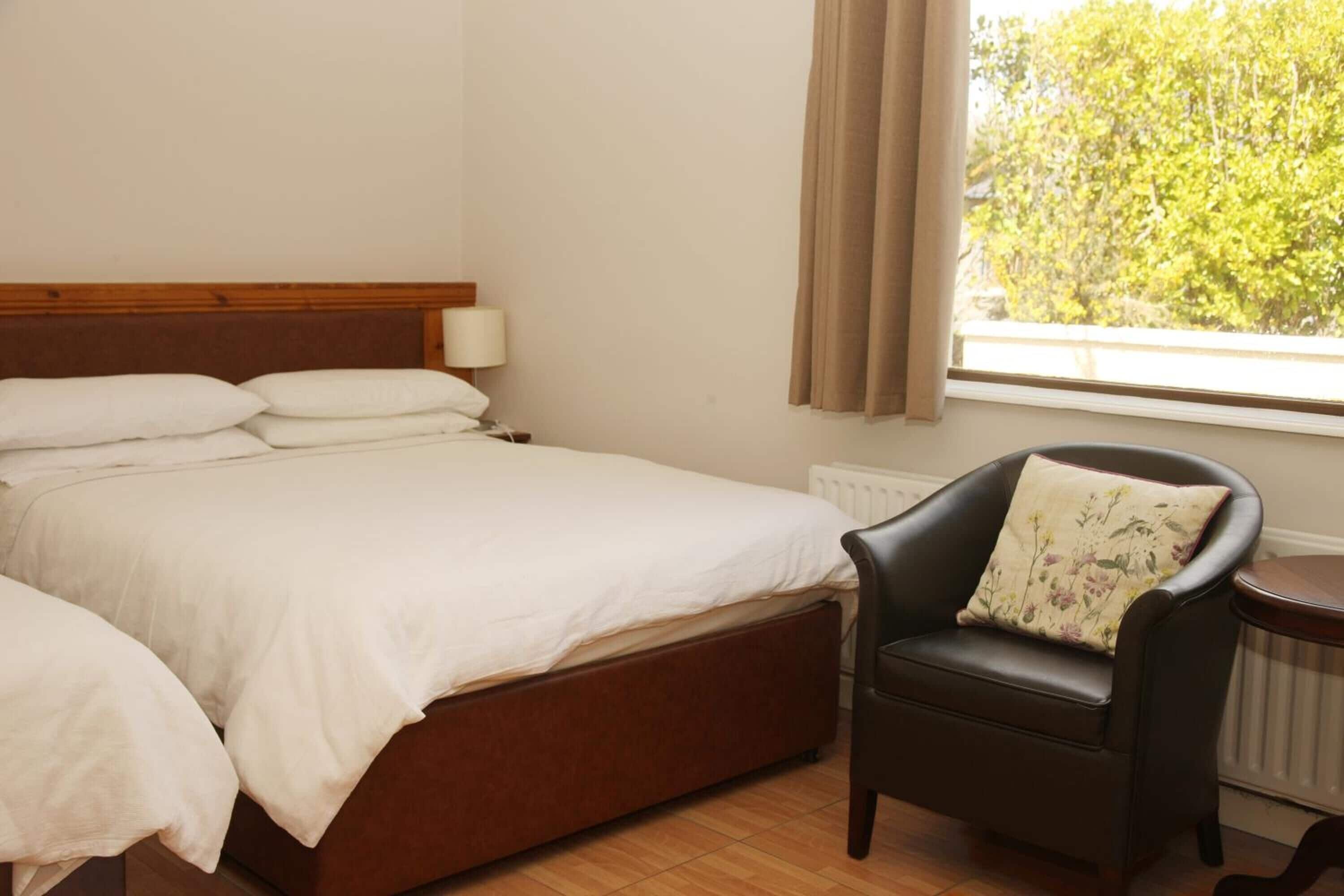 Un dormitorio con cama, una silla, una lámpara y una ventana con cortinas.