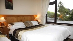 Ett hotellrum med en sänggavel i trä, två sängbord med lampor, en stor säng med vita sängkläder och ett fönster med utsikt över träd.