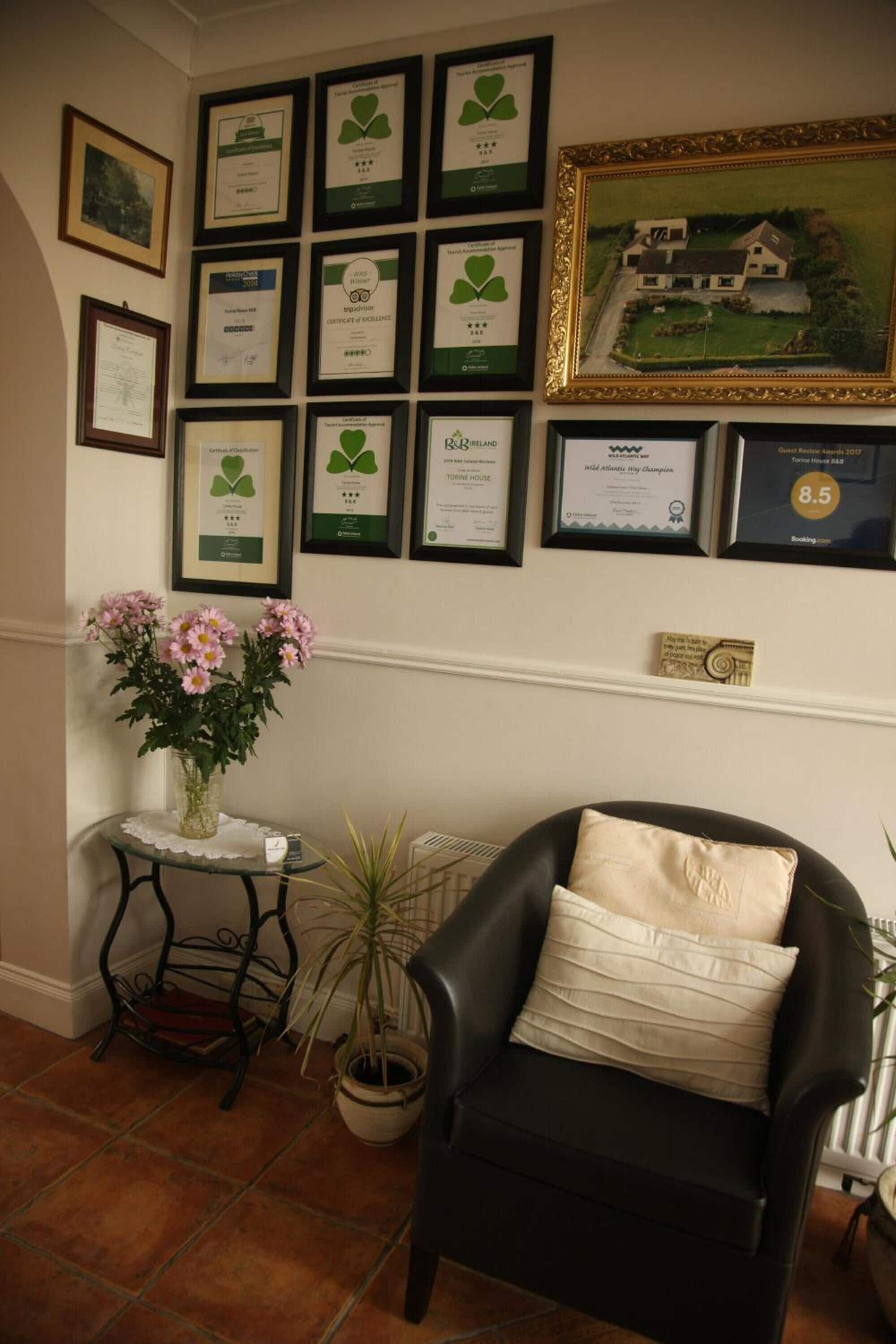 Una habitación con una butaca de cuero negro, un jarrón con flores rosadas y un diploma enmarcado en la pared.