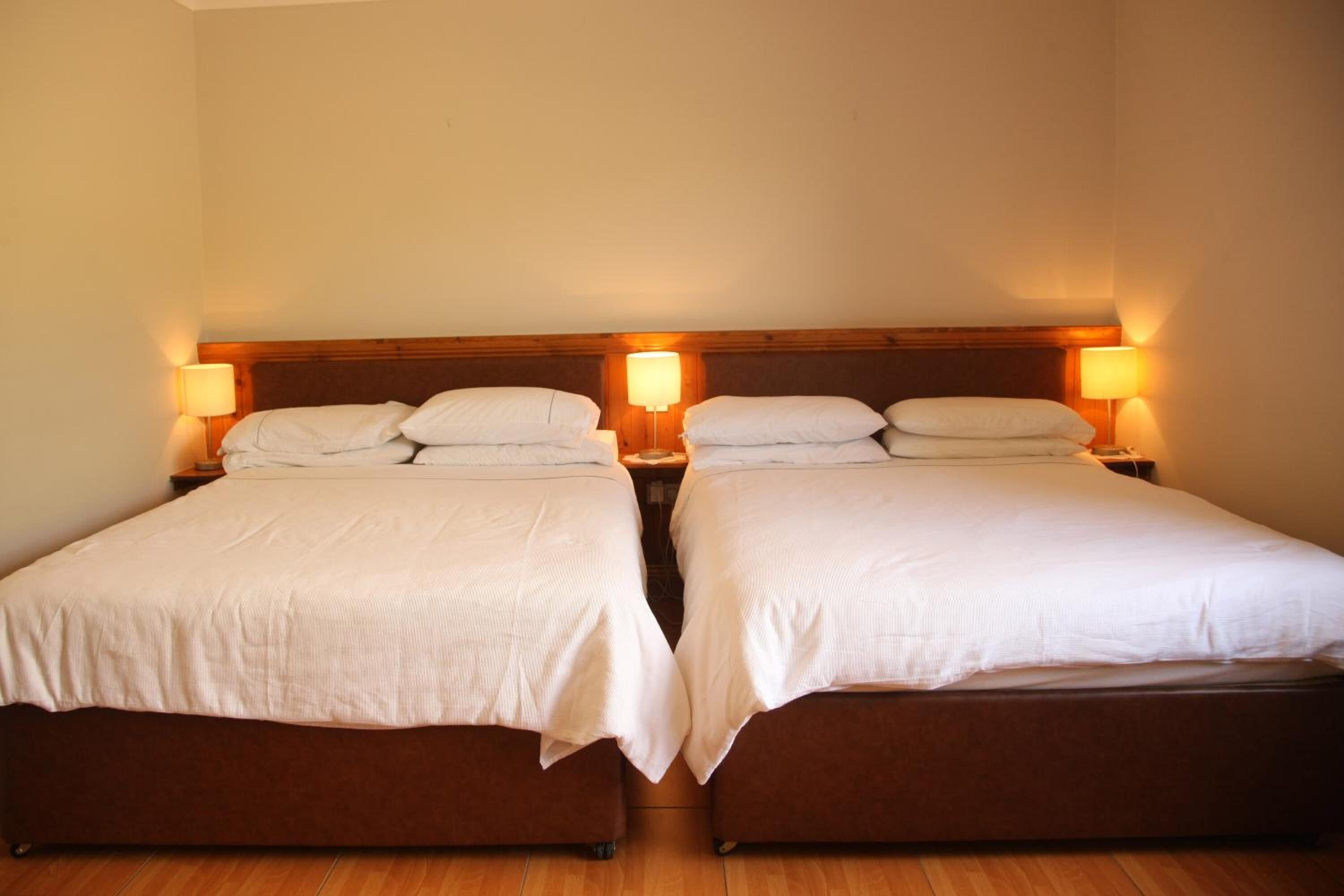 A double room with two beds, each with a wooden headboard and bedside lamps.