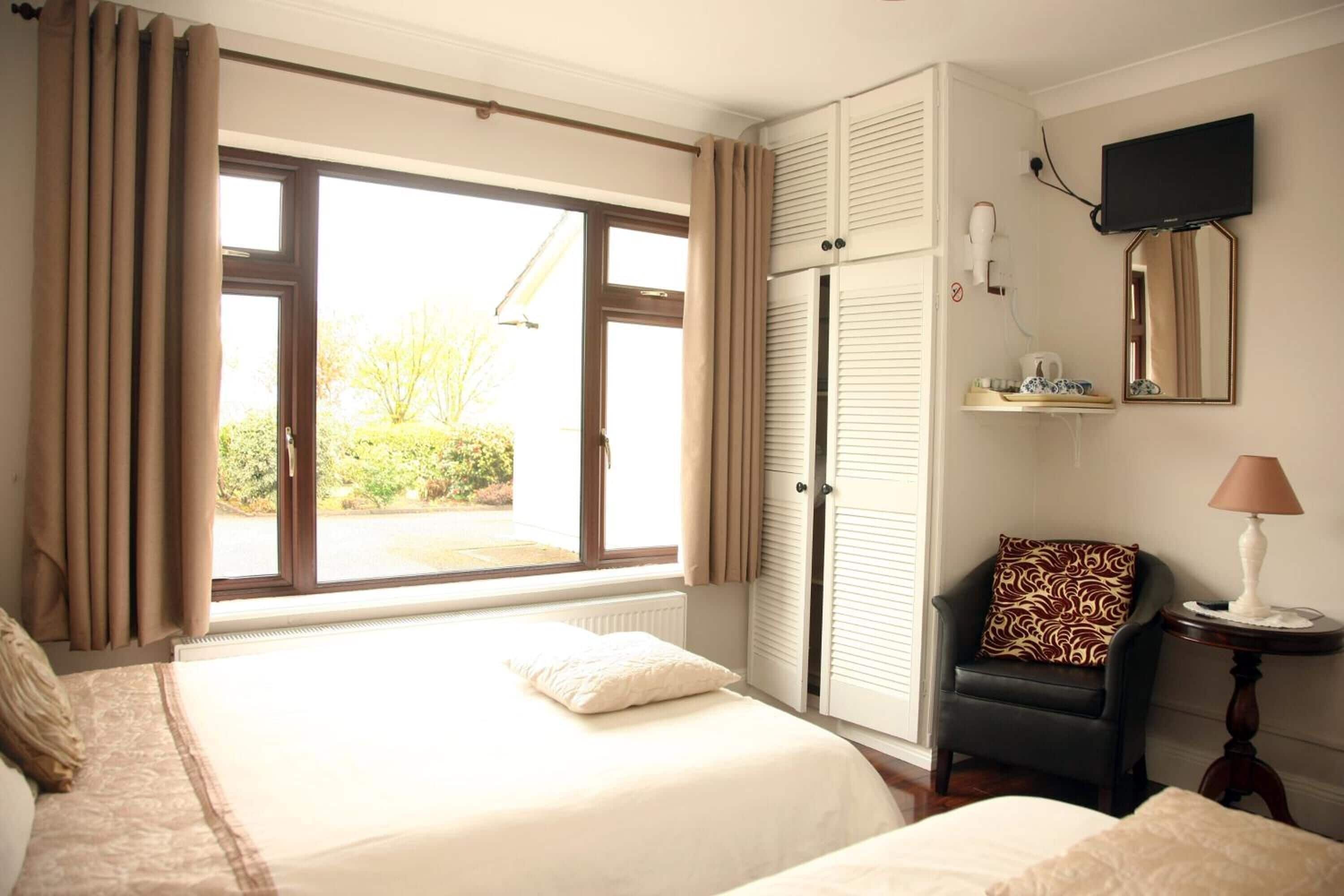 A hotel room with a bed, a chair, a TV, and a window with curtains.