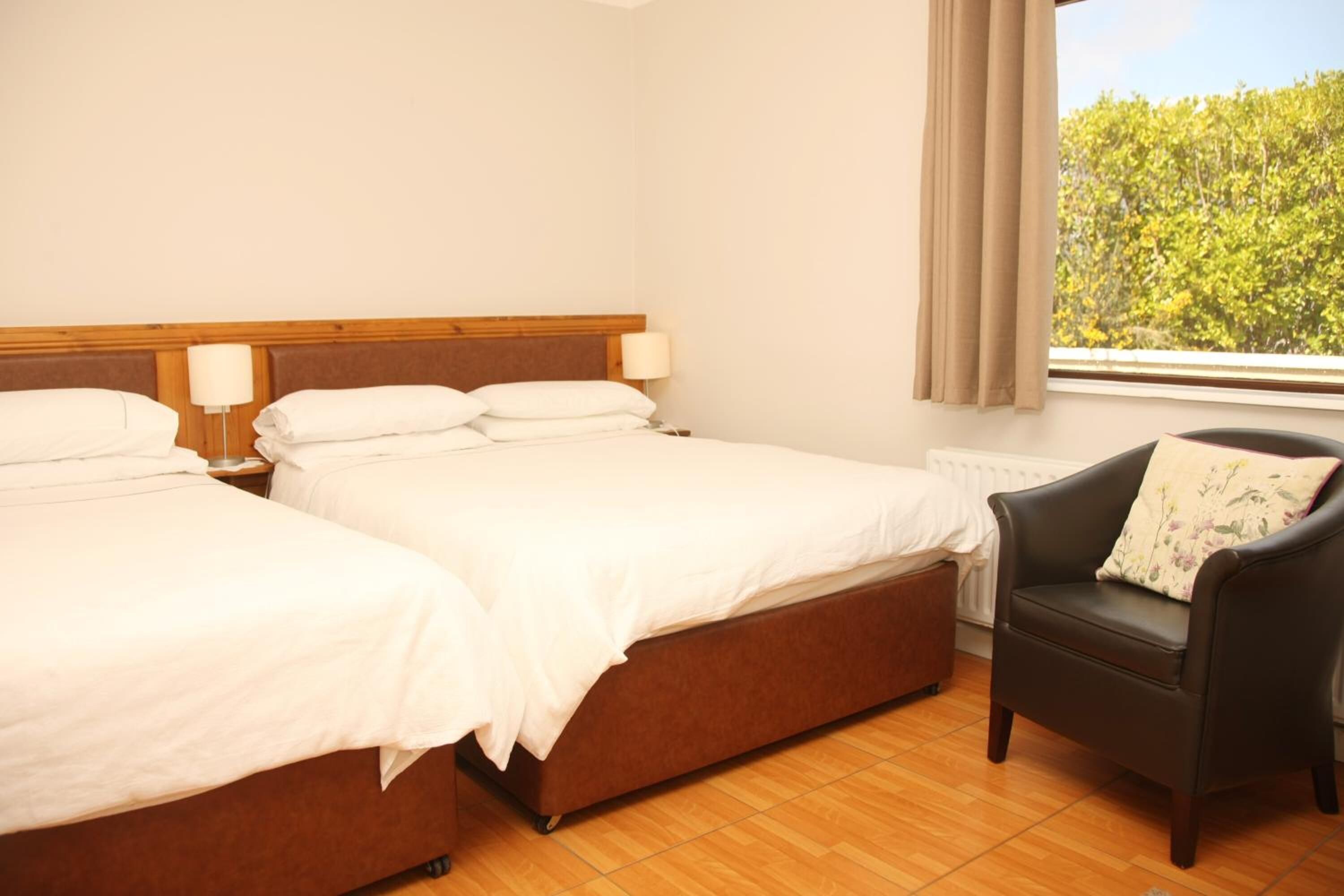 A hotel room with two beds, a chair, and a window with a view of trees.