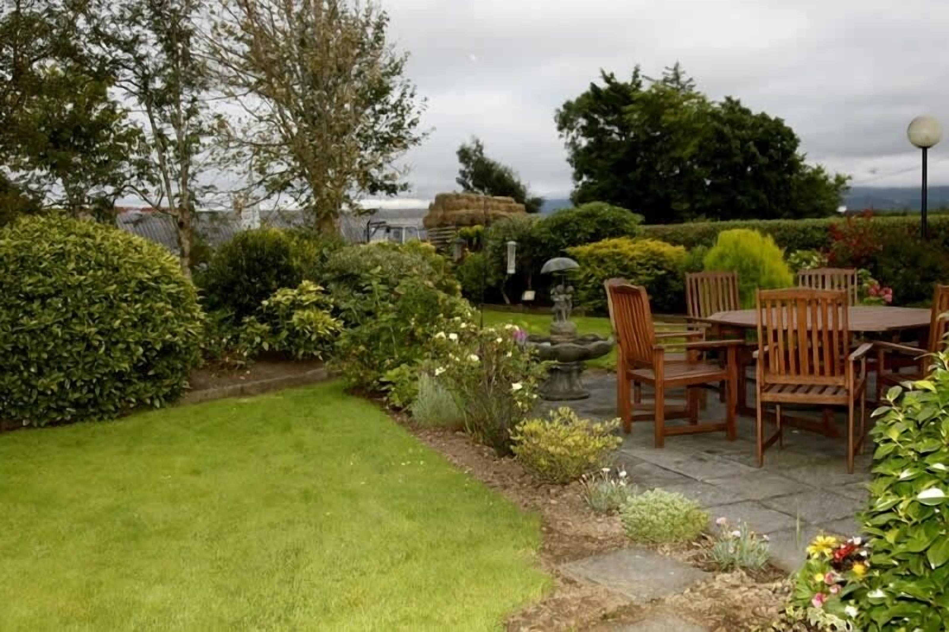 A patio area with a table and chairs, surrounded by well-maintained hedges and a variety of plants.