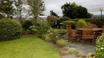 Een terras met een tafel en stoelen, omgeven door goed onderhouden hagen en diverse planten.