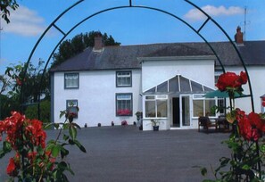 A white building with a covered patio area and a green umbrella. - Grove Farm House B&B (Inistioge)